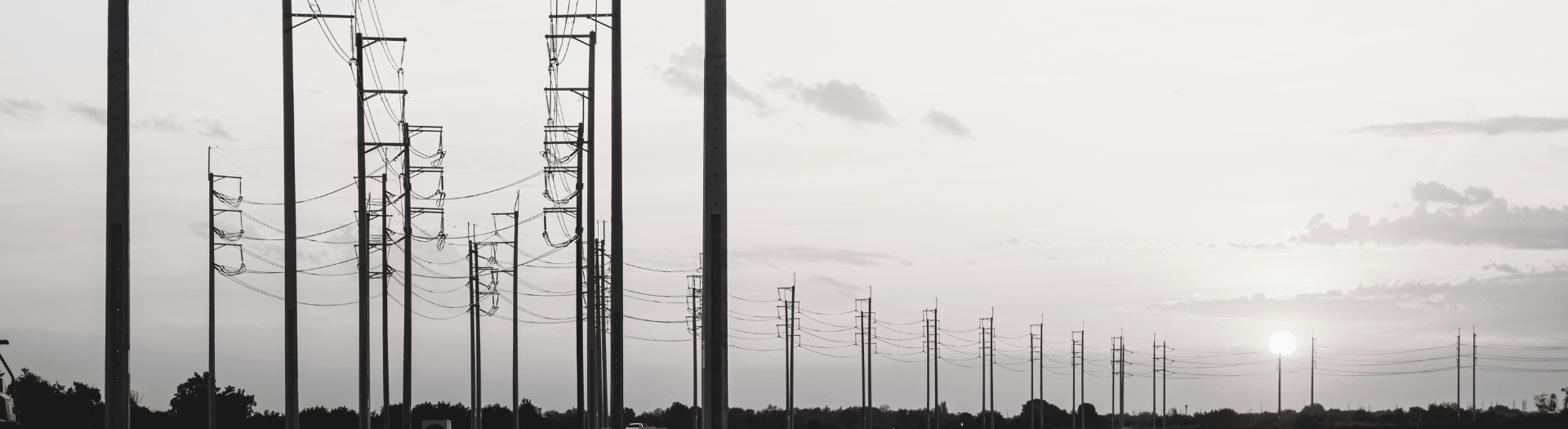 Silhouette of power lines against a setting sun, showcasing the grid's reach and infrastructure.