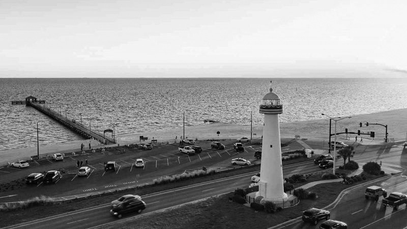 The iconic Biloxi Lighthouse stands guard on the Mississippi coast, captured in a timeless black and white aerial photo.