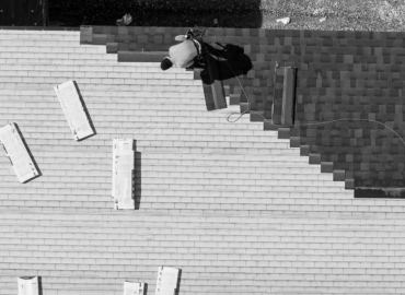 Aerial view of a roofer diligently working on a building, captured in stark black and white contrast.