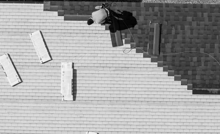 Aerial view of a roofer diligently working on a building, captured in stark black and white contrast.