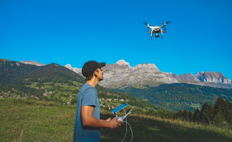 Drone operator with a remote control in a mountainous landscape, piloting a flying drone.