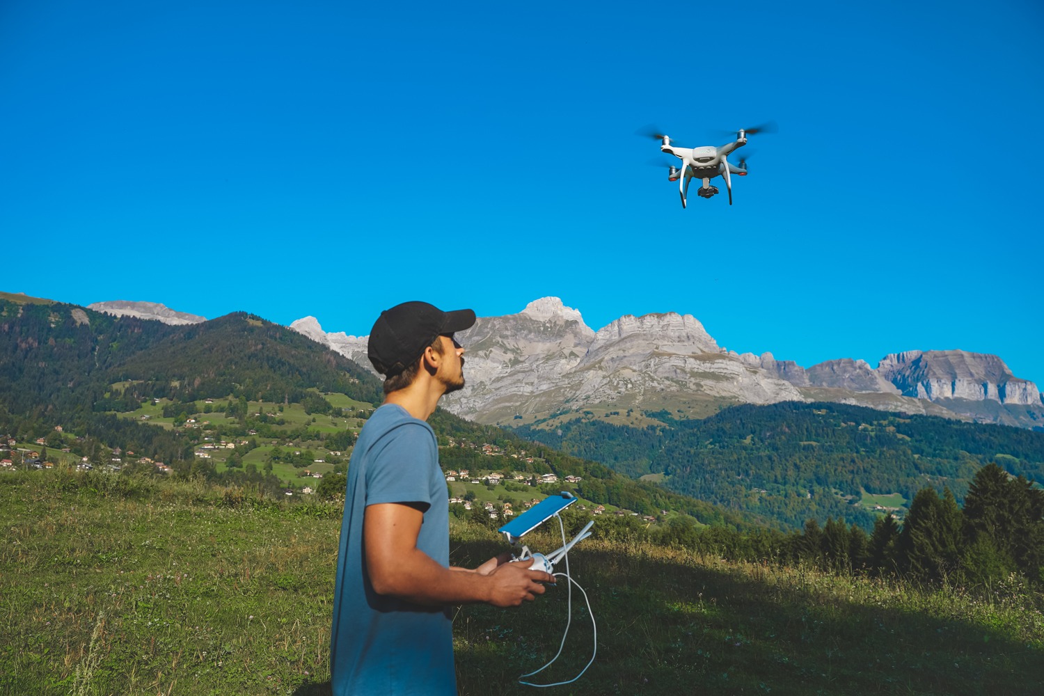 Drone operator with a remote control in a mountainous landscape, piloting a flying drone.